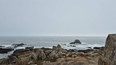 Portekiz 'in Matosinhos bölgesindeki Leca da Palmeira' daki kayalık Atlantik kıyısında dalgalar engebeli bir deniz gününde engebeli taşlara çarpıyor. Dramatik deniz manzarası doğanın gücünü ve kıyı yalnızlığını çağrıştırıyor..