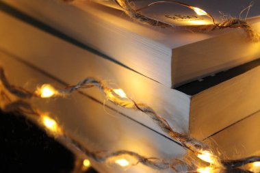 Siyah arkaplanda çelenk olan bir yığın kitap.