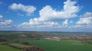 Paragliderler güzel güneşli ve kısmen bulutlu bir günde İngiliz kırsalında uçuyorlar.
