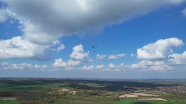 Paragliderler güzel güneşli ve kısmen bulutlu bir günde İngiliz kırsalında uçuyorlar.