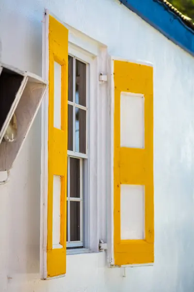 stock image A sunny and warm house facade featuring bright yellow window shutters against a crisp white wall