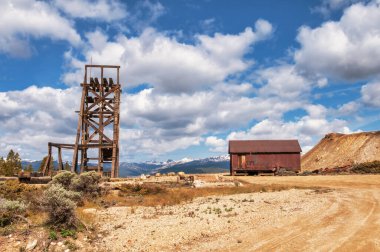 An old mining rig stands as a relic of the past in the Colorado heart land, with nature slowly reclaiming the area surrounded by mountains clipart