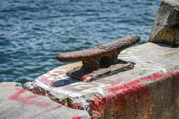 Bu görüntü eskimiş, paslanmış metal bir iskeleyi yakalıyor beton bir yüzeye sıkıca sabitlenmiş halde, sakin akan suların ve kısmen görülebilir enkazın zeminine karşı..