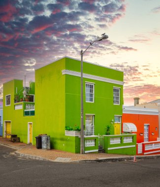 Köşedeki binalar, arka planda dramatik bir günbatımı gökyüzü, Cape Town 'da bulunan Bo-Kaap Güney Afrika' nın kültürel mekanında mimari güzellikler ve canlı renkler sergiliyor..