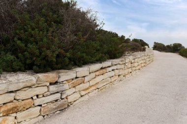 Her iki tarafında duvarlar ve önünde ağaçlar olan antik bir Kıbrıs 'a giden taştan bir yol. Gökyüzü bulutlu..
