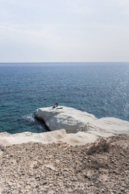 Kıbrıs 'ın mavi denizi yakınlarındaki dev beyaz kayanın üzerinde oturan ve balık tutan adam