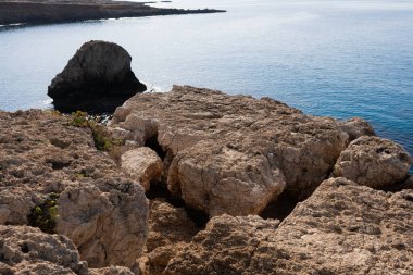 Taşları ve taşları olan yaz plajı. Temiz su ve mavi. Adriyatik Denizi 'nin sularındaki taş yığınlarının üzerine kısmen gölge, kısmen güneş ışığı ile aydınlanan devasa mavi kayaların yakınındaki gökyüzüne bak