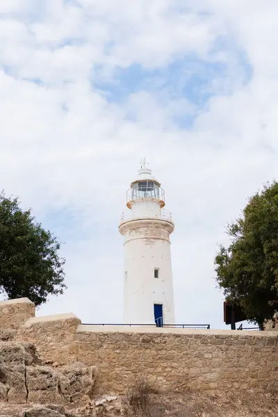 Ağaçlarla çevrili bulutlu bir gökyüzünün altında beyaz deniz feneri var.