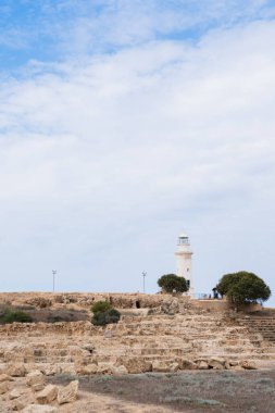 Ağaçlarla çevrili bulutlu bir gökyüzünün altında beyaz deniz feneri var.