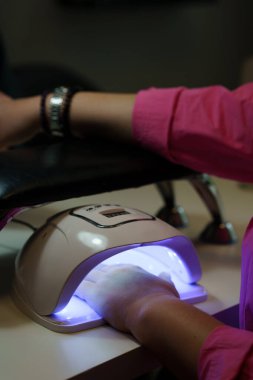 Manikür salonunda kırmızı cila sürmüş bir müşteri tırnaklarının ultraviyole ışıkta kurumasını bekliyor..