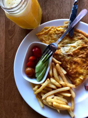 Patates kızartmalı kahvaltı tabağı, taze salatalıklı yumurta ve vişneli domates ve portakal suyu.