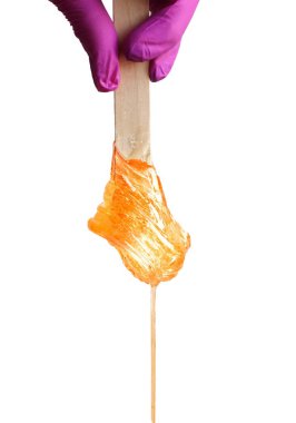 Pembe eldivenli bir kadın eli beyaz arka planda tüy dökmek için sarı şeker ya da balmumu içeren tahta bir sopa tutar. Epilasyon, tüy dökücü, tüy dökücü, güzellik..