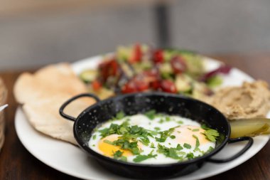 Yoğurtlu Türk yumurtaları, kokulu tereyağı, bezelye filizi, yassı ekmek ve çay. Haşlanmış yumurta ve sıvı yumurta ile geleneksel Türk kahvaltısı. Seçici odak, yakın plan.