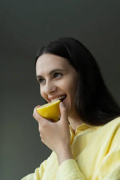 Gri arka planda yeşil limon tutan neşeli genç bir kadının portresi.