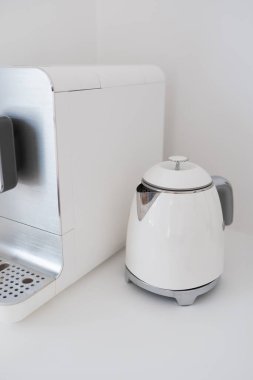 Beyaz bir masanın üstündeki beyaz kahve makinesi ve su ısıtıcısının ayrıntıları.