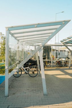 Bisiklet parkında parlayan bükülmüş tüplerden yapılmış bisiklet tezgahları var. Bisikleti meydana yerleştirmek ve kilitlemek için. Birbirine kenetlenmiş asfalt ve çizgili granit küpler. kırmızı, gri, sarmal