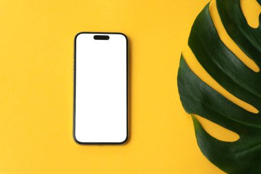 Sarı arkaplanda beyaz beyaz ekranlı sahte telefon, canavar yaprağı, reklam için düzen, metin için kopyalama alanı