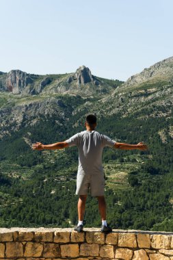 Sıradan bir adam dışarıda, yeşil dağ manzarasında dikiliyor. Resim seyahat, macera veya özgürlük kavramları için uygundur..