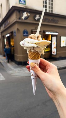 Kadın elinde külahta vanilyalı ve çikolatalı dondurma. Açık hava ortamında yiyecek, tatlı, sosyal medya içeriği, menü veya seyahat bağlamında.