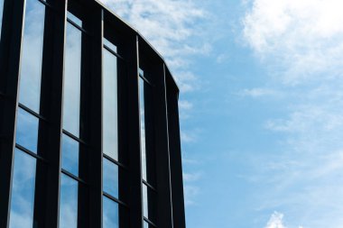 Büyük cam pencereli, mavi gökyüzünü ve bulutları yansıtan uzun ve modern bir bina. Mimari, kentsel gelişim veya iş kavramlarını resmetmeye elverişli.