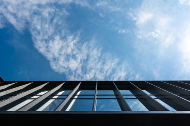 Büyük cam pencereleri ve metal kirişleri olan çağdaş mimari, parlak bir gökyüzünün altında alçak açı. Kentsel gelişimi, modern yapıyı veya mimari tasarım kavramlarını resmetmeye elverişli.