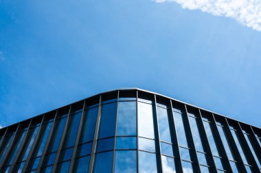 Dikey metal çerçeveli çağdaş cam cephe açık mavi gökyüzünü ve bulutları yansıtır. Mimari, iş veya kentsel gelişim kavramlarını resmetmeye elverişli.