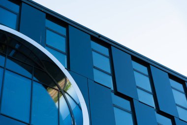 Çağdaş ofis ön cephesinde büyük dairesel mimari detaya sahip mavi renkli cam paneller ve dikdörtgen pencereler yer alıyor. Modern mimari, iş ortamları ve kentsel kalkınma kavramlarını resmetmeye uygundur.