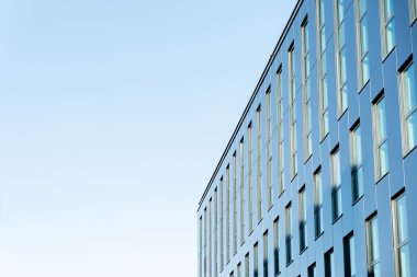 Yansıtıcı cam pencereleri ve temiz çizgileri olan çağdaş ofis binası, açık mavi gökyüzüne karşı kurulmuş. İş, mimari veya kentsel gelişim kavramlarını resmetmeye uygundur.