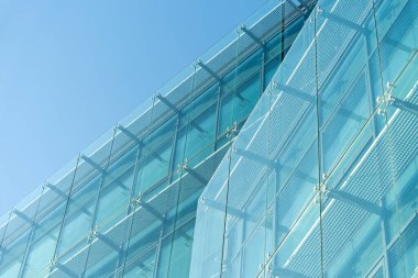 Şeffaf cam paneller ve temiz mavi gökyüzü altında metal iskelet içeren çağdaş mimari yapı. Modern mimari, inşaat veya kentsel tasarım kavramlarını resmetmeye elverişli.