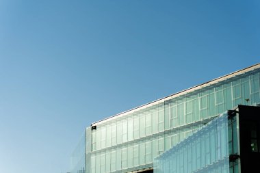 Temiz çizgileri ve açık mavi gökyüzünün altındaki yansıtıcı pencereleri olan çağdaş cam ofis binası. Mimari, iş veya kentsel gelişim kavramlarını resmetmeye elverişli.