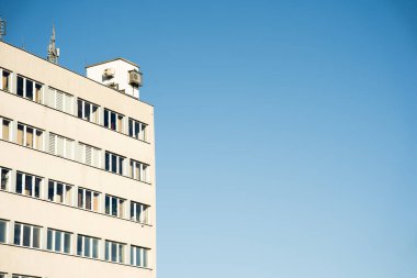 Birden fazla penceresi ve çatısı olan dikdörtgen ofis binası, açık mavi gökyüzüne karşı kurulmuş. Kentsel mimari, iş ortamları veya şehir altyapı kavramlarını resmetmeye elverişli.