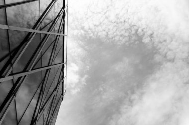 Sol tarafta sağda bulutlu bir gökyüzü ile tezat oluşturan geometrik metal çerçeve ile çağdaş cam bina cephesi gösterilmektedir. Mimari, kentsel tasarım veya modern inşaat kavramları için uygun.