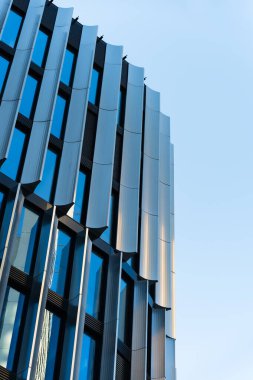 Dışarıdaki modern ofis binası yansıtıcı mavi camlı pencereler, mavi gökyüzünde dikey metal paneller. Modern mimariyi, kentsel gelişimi veya ticari gayrimenkul kavramlarını resmetmek için.