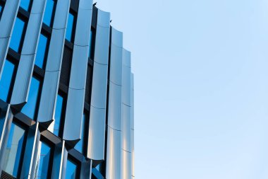 Çağdaş ofis binası yansıtıcı cam pencereli, metalik cepheli, açık mavi gökyüzünde. Kentsel mimariyi, iş ortamlarını ve modern şehir kalkınma kavramlarını resmetmek için.