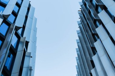 Mavi cam cepheli ve metalik mimari panelli iki uzun modern bina alçak açıdan gösteriliyor. Kentsel mimariyi, şehir gelişimini veya modern inşaat kavramlarını resmetmeye elverişli.