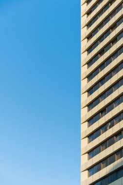 Tekrarlanan pencereleri ve bej cepheli, açık bir günde mavi gökyüzü arkaplanıyla çekilen uzun modern bir bina. Kentsel mimari, gayrimenkul veya şehir kalkınma temaları için elverişli.