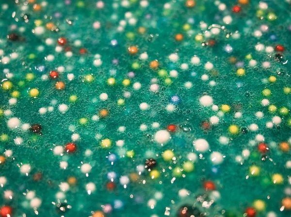 Rainbow beads mixed into blue green colored slime - close up shot for backgrounds to add your own text.
