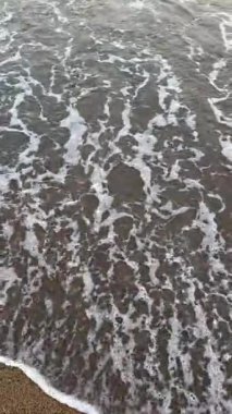 Yumuşak deniz dalgaları güneş ışığı altında kumlu kıyıya yavaşça yuvarlanıyor. Yüksek kalite 4k görüntü