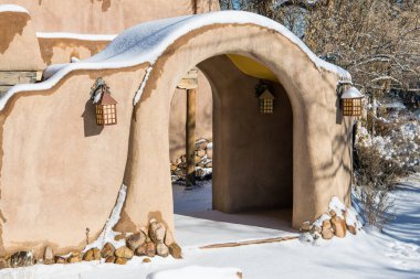 Karlı kış manzarası, Santa Fe, New Mexico 'da kemerli girişi olan karla kaplı bir kerpiç duvarı.