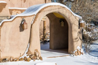 Snowy winter scene of a snow-covered adobe wall with an arched entrance in Santa Fe, New Mexico clipart