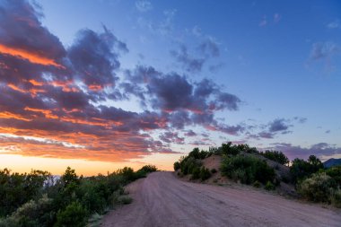 Pembe ve mor bulutlu dramatik bir günbatımı gökyüzünün altındaki tepeye uzanan kirli bir yol.