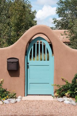 Turquoise gate in an arched entrance to a garden through an adobe wall in Santa Fe, New Mexico clipart