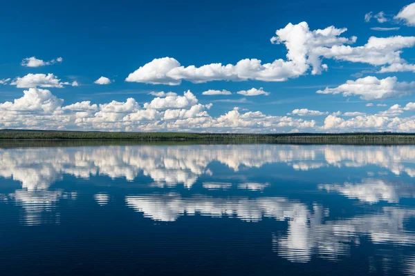 stock image Peaceful, idyllic scene of blue sky and fluffy white clouds reflected in the waters of a perfectly still lake