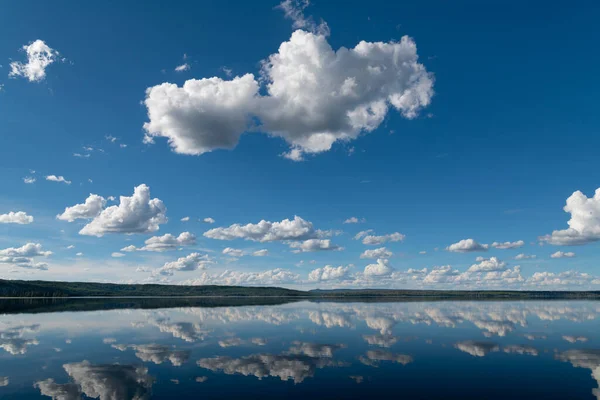 Mavi gökyüzü ve tüylü beyaz bulutların durgun gölün sularına yansıdığı huzurlu, huzurlu bir manzara.
