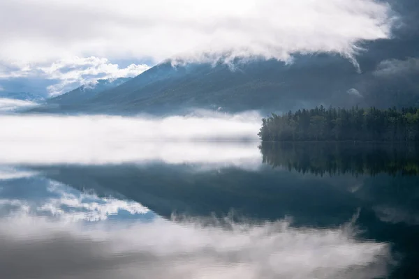 Sisli dağların ve ormanın huzurlu manzarası McDonald Gölü, Buzul Ulusal Parkı, Montana 'daki bir alp gölüne yansıyor.