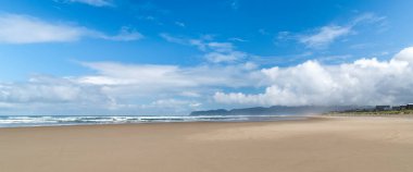 Beyaz fırtına bulutlu mavi gökyüzü altında McPhillips Plajı, Oregon 'da büyük kumlu bir sahil manzarası.