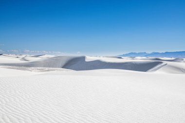 Beyaz kum tepeleri ve New Mexico 'daki White Sands Ulusal Parkı' ndaki uzak dağlardan oluşan geniş, çorak bir arazi.