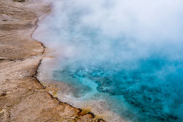 A beautiful pool of clear water and steam forms abstract scene with hues of blue and turquoise at Excelsior Geyser, Yellowstone National Park, Wyoming