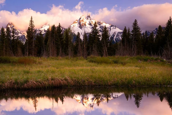 Karlı dağ tepelerinde gün doğumu ve güzel pembe ve mor bulutlar Grand Teton Ulusal Parkı, Wyoming 'deki durgun bir gölete yansıyor.