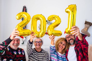 2021 yılının dört balon numarasını elinde tutarak evde eğlenen ve gülümseyen dört kişi. Aile gülüyor, Noel ve yeni yılı kutluyor. 